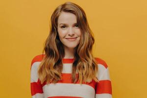 Smiling woman with flowing hair wearing a striped sweater, her contented expression a burst of warmth against a yellow backdrop. photo