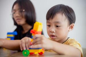 Asian cute brother and sister play with a toy block designer on the table in the living room at home. Concept of siblings bonding, friendship, and learning through play activity for kid development. photo