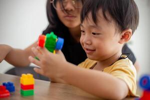 asiático linda hermano y hermana jugar con un juguete bloquear diseñador en el mesa en el vivo habitación a hogar. concepto de hermanos unión, amistad, y aprendizaje mediante jugar actividad para niño desarrollo. foto