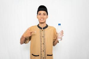 Muslim Asian man wearing Muslim clothes showing mineral water in a bottle. Isolated white background. photo