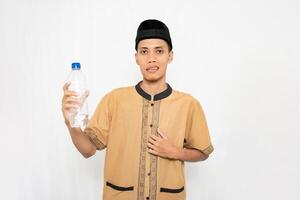 Asian Muslim man wearing Muslim clothes carrying mineral water in a bottle. Isolated white background. photo