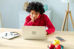 africano americano niña utilizando ordenador portátil a hogar oficina mirando a pantalla mecanografía chateando leyendo escritura correo electrónico. joven mujer teniendo virtual reunión en línea charla vídeo llamada conferencia. trabajo aprendizaje desde hogar foto