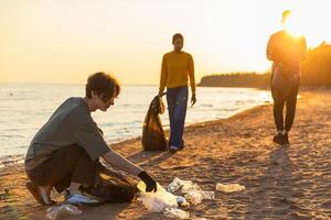 tierra día. voluntarios activistas equipo recoge basura limpieza de playa costero zona. mujer mans pone el plastico basura en basura bolso en Oceano costa. ambiental conservación costero zona limpieza foto