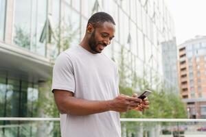 African american man holding smartphone touch screen typing scroll page on urban street in city. Guy with cell phone surfing internet using social media apps shopping online. Cellphone addiction photo