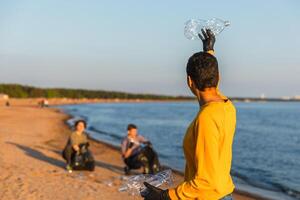 tierra día. voluntarios activistas equipo recoge basura limpieza de playa costero zona. mujer pone el plastico botella basura en basura bolso en Oceano costa. ambiental conservación costero zona limpieza foto