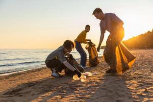 Earth day. Volunteers activists team collects garbage cleaning of beach coastal zone. Woman mans puts plastic trash in garbage bag on ocean shore. Environmental conservation coastal zone cleaning photo