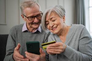 mayor Pareja hombre mujer compras en línea con teléfono inteligente pago con crédito tarjeta. antiguo personas comprando en Internet entrar crédito tarjeta detalles a hogar adentro. en línea compras entrega Servicio comercio electrónico foto