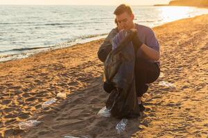 Earth day. Volunteers activists collects garbage cleaning of beach coastal zone. Man puts plastic trash in garbage bag on ocean shore. Environmental conservation coastal zone cleaning photo