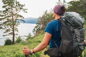 Hiking tourism adventure. Backpacker hiker man looking at beautiful view. Hiker tourist with backpack walking in green forest near lake. Back view man enjoy hike trekking tourism active vacation photo