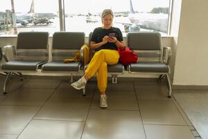 aeropuerto Terminal. mujer esperando para vuelo utilizando teléfono inteligente niña con célula teléfono en aeropuerto surf Internet social medios de comunicación aplicaciones de viaje hembra en embarque salón de aerolínea centro. de viaje niña foto