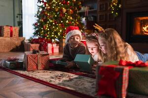 Merry Christmas Xmas holiday. Children unpacking open up gift box near Christmas tree. Kids in living room with Christmas tree fireplace opening gift box with surprise faces. Christmas eve at home photo