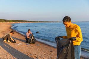 Earth day. Volunteers activists collects garbage cleaning of beach coastal zone. Woman and mans puts plastic trash in garbage bag on ocean shore. Environmental conservation coastal zone cleaning photo