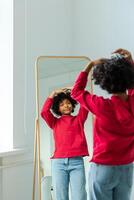 Love yourself. Beautiful young smiling african american woman dancing touching curly hair enjoying her mirror reflection. Black lady looking at mirror looking confident and happy. Self love concept photo