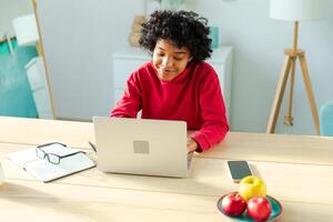 africano americano niña utilizando ordenador portátil a hogar oficina mirando a pantalla mecanografía chateando leyendo escritura correo electrónico. joven mujer teniendo virtual reunión en línea charla vídeo llamada conferencia. trabajo aprendizaje desde hogar foto