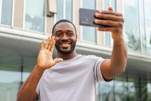 African American man holding smartphone having video chat on urban street in city. Guy blogger chatting with best friends in social network. Man having virtual meeting online chat video call outdoor photo