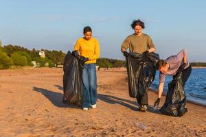 tierra día. voluntarios activistas equipo recoge basura limpieza de playa costero zona. mujer mans con basura en basura bolso en Oceano costa. ambiental conservación costero zona limpieza foto