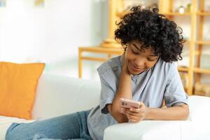 African girl holding smartphone touch screen typing scroll page at home. Woman with cell phone surfing internet using social media apps playing game. Shopping online Internet news cellphone addiction photo