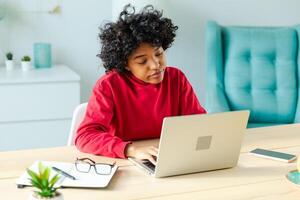 africano americano niña utilizando ordenador portátil a hogar oficina mirando a pantalla mecanografía chateando leyendo escritura correo electrónico. joven mujer teniendo virtual reunión en línea charla vídeo llamada conferencia. trabajo aprendizaje desde hogar foto