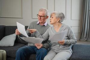 Sad tired disappointed middle aged senior couple sit with paper document. Unhappy older mature man woman reading paper bill managing bank finances calculating taxes planning loan debt pension payment photo