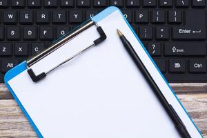 Home office workspace with black keyboard, blue clipboard and pen. Flat lay, top view photo