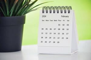 February 2024 desk calendar with potted plant on a desk with green background. photo