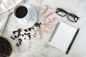 Cup of coffee and coffee beans background with measure tap and notebook. photo