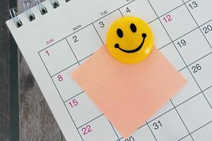 Orange paper sticky note with smiley face and stuck to a calendar background. photo