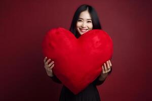 ai generado sonriente asiático mujer participación grande rojo corazón almohada en oscuro rojo fondo, neural red generado fotorrealista imagen foto