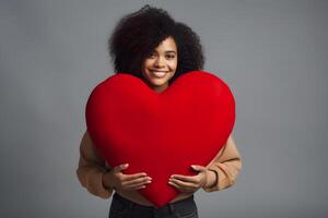 AI generated mixed race woman holding big red heart on gray background, neural network generated photorealistic image photo