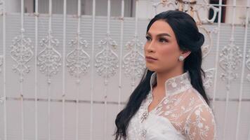 Elegant woman in white dress posing by ornate gate, serene expression, outdoor setting. video