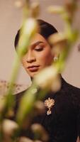 Elegant woman in black attire with a brooch, partially obscured by blurred greenery in the foreground. video
