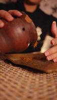 Close-up of hands grating tobacco with a wooden grater over a woven mat, with a rustic and traditional kitchen setting. video