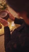 Elegant person in traditional attire holding a cup, with a serene expression, standing by a table with decorative elements. video