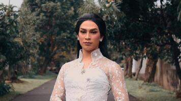 Elegant person in a white lace dress standing on a garden path with trees video