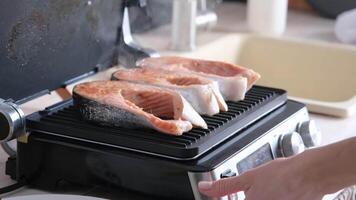 Woman cooking salmon steaks on modern electric grill in the kitchen video