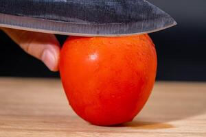 hembra manos participación un cuchillo y rebanar Tomates en un de madera el cortar tablero. cortar Fresco rojo Tomates cerca arriba. foto