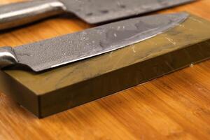 Sharpening knives with a Whetstone. Knife sharpening. Sharp knife and sharpening stone on a wooden cutting board. photo