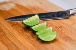 A lime sliced in quarters and placed on a wooden cutting board next to kitchen knife. Hight Vitamin C Natural photo