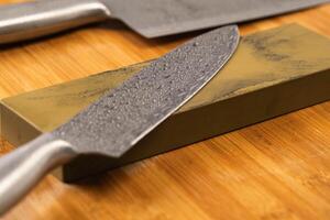 Sharpening knives with a Whetstone. Knife sharpening. Sharp knife and sharpening stone on a wooden cutting board. photo