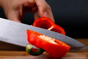 manos corte rojo campana pimientos en un de madera el cortar tablero. mujer el cortar campana pimientos en cocina cerca arriba. foto