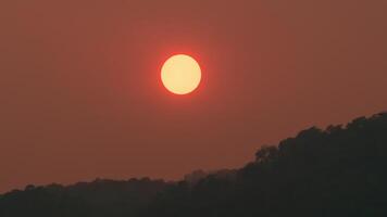 Time lapse of the sun setting over hills that are covered with clouds, in the style of smokey background. video