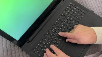 een gepensioneerde leert naar werk Aan een laptop. groen scherm monitor. laptop met groen scherm chromatisch toetsenbord en mollig vrouw handen. video