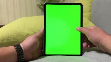 Man at home with tablet computer with green screen. Video of green smartphone screen mockup. Selection of purchases in an online store. Season of discounts and gift shopping.