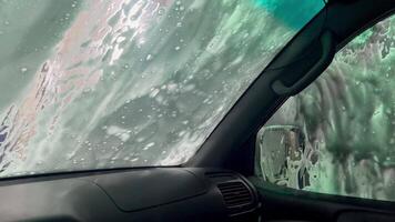 View of an automatic car windshield wash with foam Automatic car wash view from the car cabin. Sliding foam from the windshield. View from inside. Time to wash the car. video