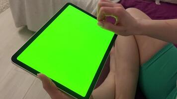 ein Frau im das Lotus Position wählt etwas auf Grün Bildschirm Video. Digital Tablette mit Grün Bildschirm chromatisch Tastatur im das Hände von ein Mädchen. video