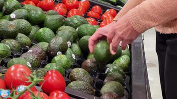 23.10.23 mississauga canadá-caucásico mujer 50-55 años antiguo elige aguacate. apetitoso aguacate en un Tienda estante de cerca. video