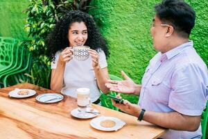 sonriente amigos hablando y disfrutando café a un mesa. concepto de amigos disfrutando un bueno café. dos contento amigos teniendo un café y hablando foto