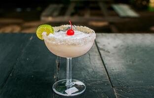 Frozen coconut cocktail with cherry on top on wooden table. Coconut margarita with cherry on wooden table. photo