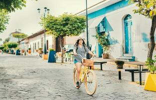 hermosa y contento niña montando un bicicleta en el calle de la calzada, granada, Nicaragua. turista mujer montando un bicicleta en el calles de granada foto