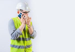 Male engineer talking on the phone secretly isolated. Young engineer in helmet talking on cell phone in silence, covering mouth photo